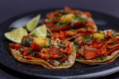 Mexican themed party tray food set-up being displayed. Pork tacos with lime and pineapple, coriander and onion on a black plate.